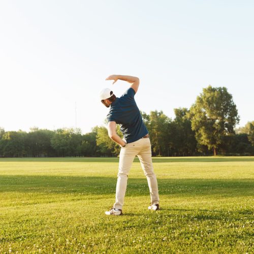 Young male golfer stretching muscles before starting the game at the green field