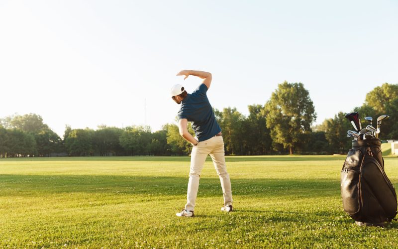 Young male golfer stretching muscles before starting the game at the green field